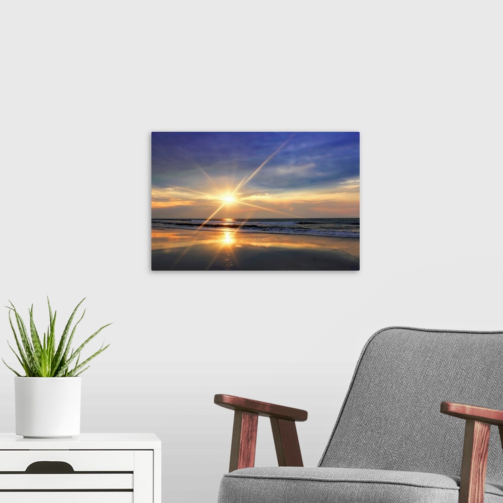 A modern room featuring The sunrises over the ocean and reflects on the waves of a sandy beach in this landscape photograph.