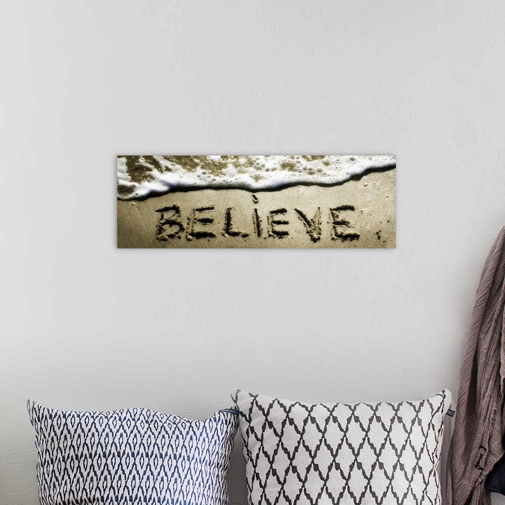 A bohemian room featuring The word "Believe" drawn in the sand near the ocean water.