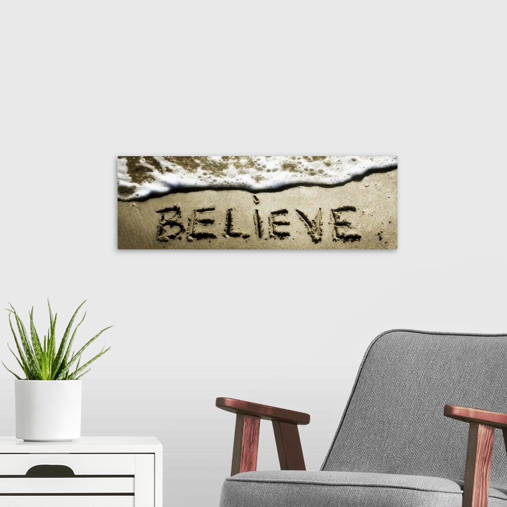 A modern room featuring The word "Believe" drawn in the sand near the ocean water.