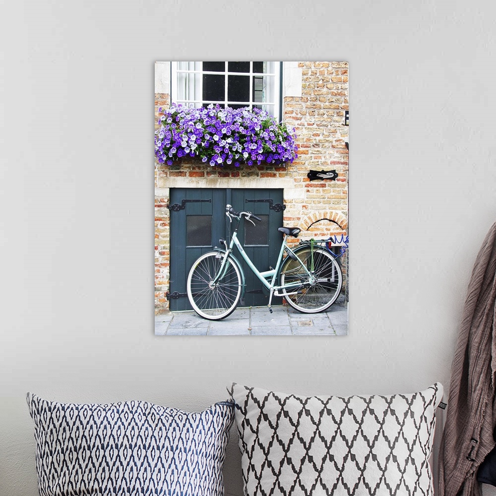 A bohemian room featuring A bicycle parked near a small door with a flowerbox full of purple flowers overhead.