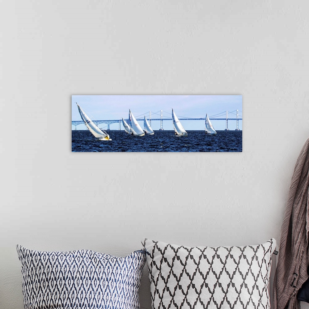 A bohemian room featuring A group of sailboats on the water in front of a long bridge.