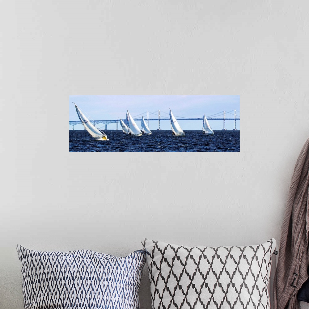 A bohemian room featuring A group of sailboats on the water in front of a long bridge.