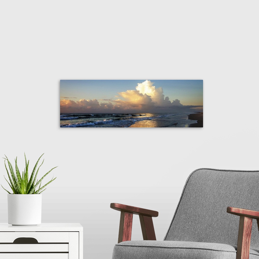 A modern room featuring Panoramic photograph of the ocean at sunrise with fluffy clouds in the sky and shorebirds in the ...