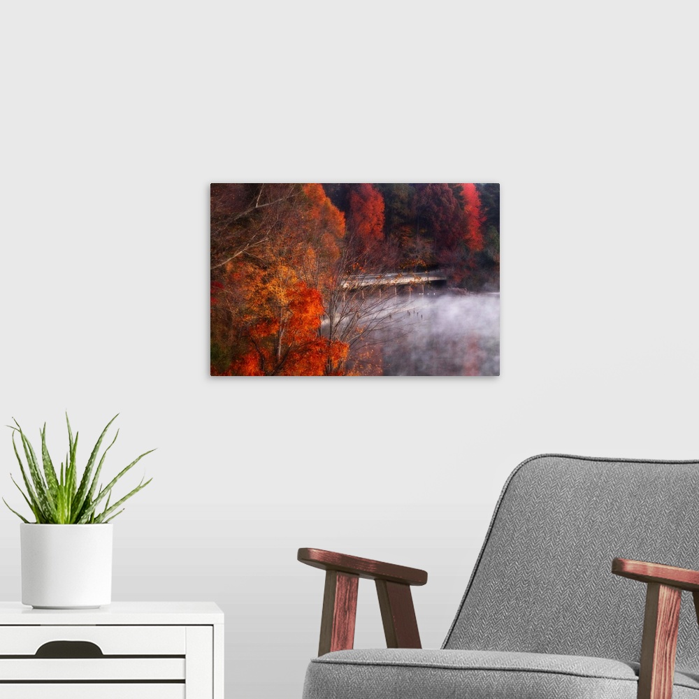 A modern room featuring Landscape photograph on a big canvas of a low mist hanging over the water, beneath a bridge surro...