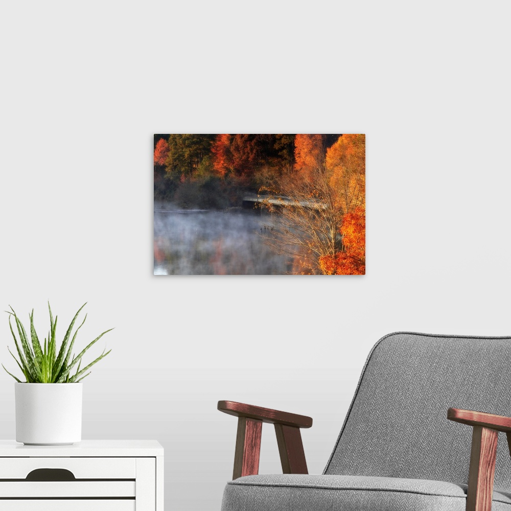A modern room featuring Giant horizontal photograph of vivid fall colored trees surrounding a bridge, as a fog rises from...