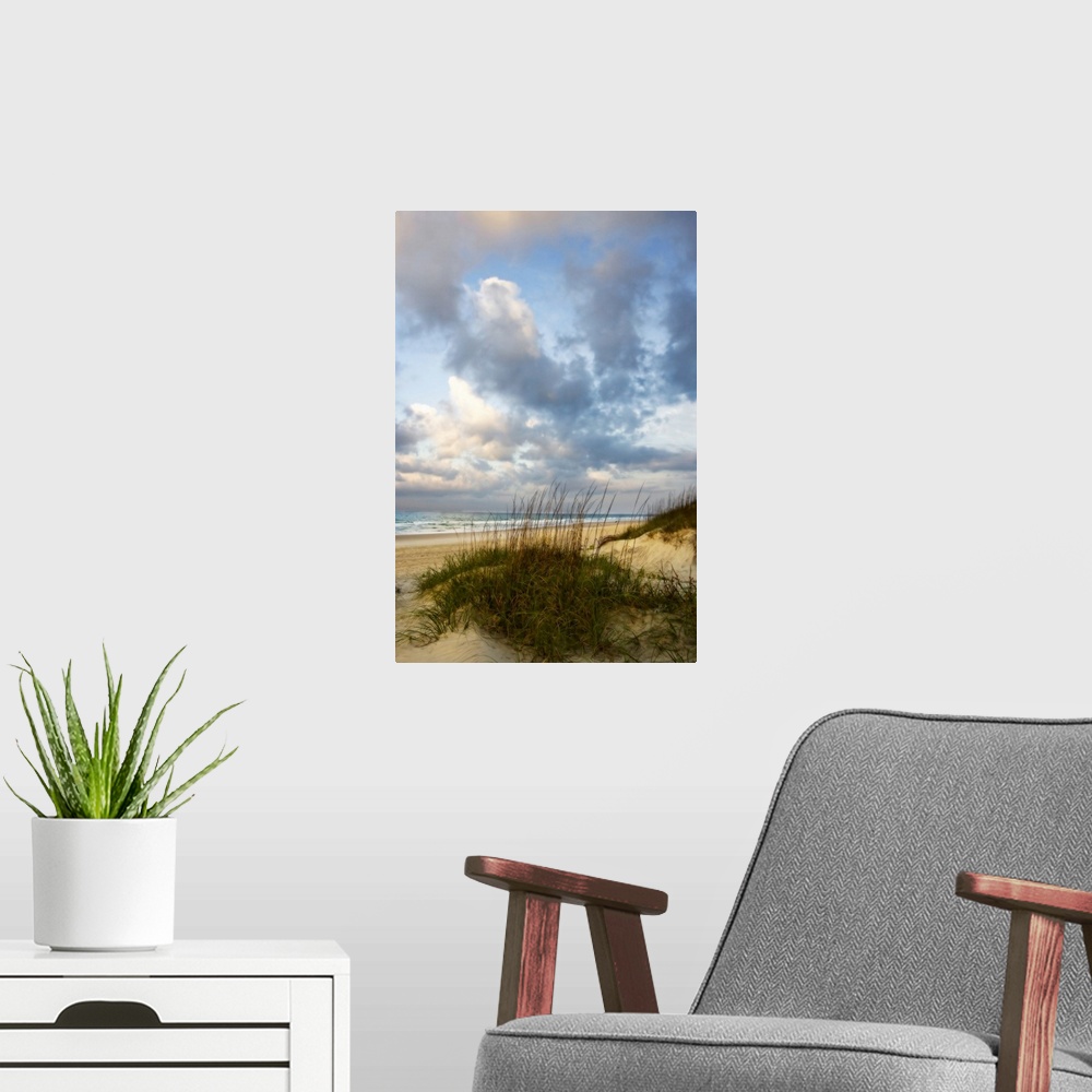 A modern room featuring Vertical photograph of grassy dunes in front of the beach, beneath a sky of billowing clouds as t...