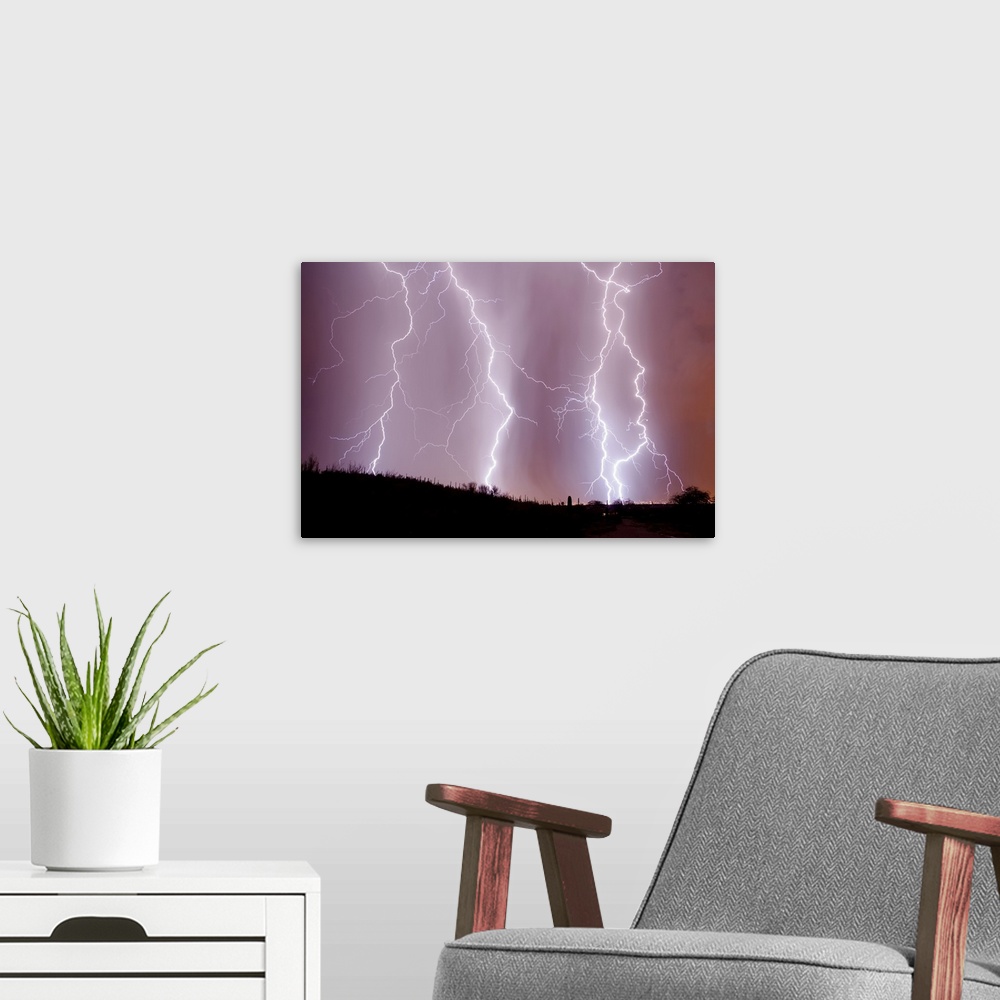 A modern room featuring Photograph of three large lightning bolts striking down in an orange, purple, and pink sky above ...