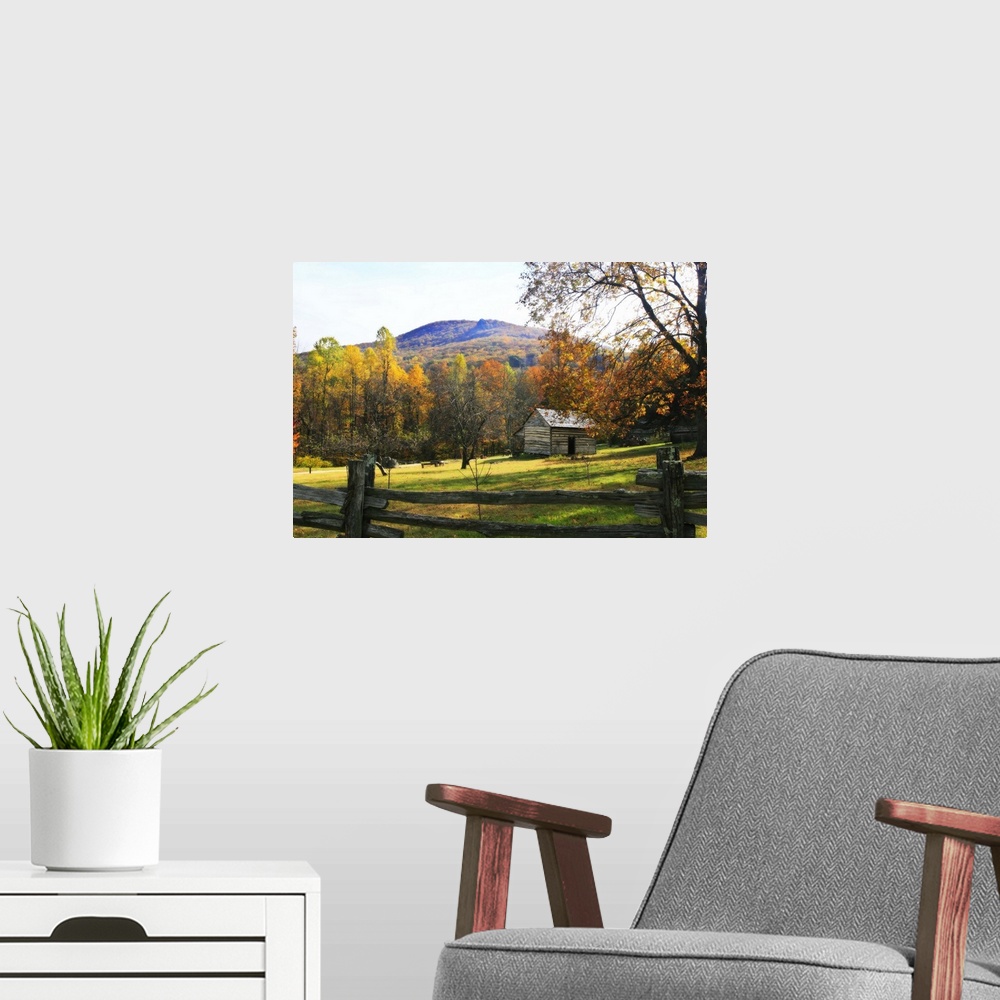 A modern room featuring This is a landscape photograph of a log cabin in a meadow surrounded by autumn trees behind a pri...