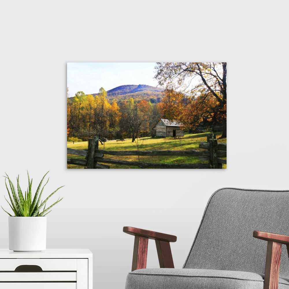 A modern room featuring This is a landscape photograph of a log cabin in a meadow surrounded by autumn trees behind a pri...