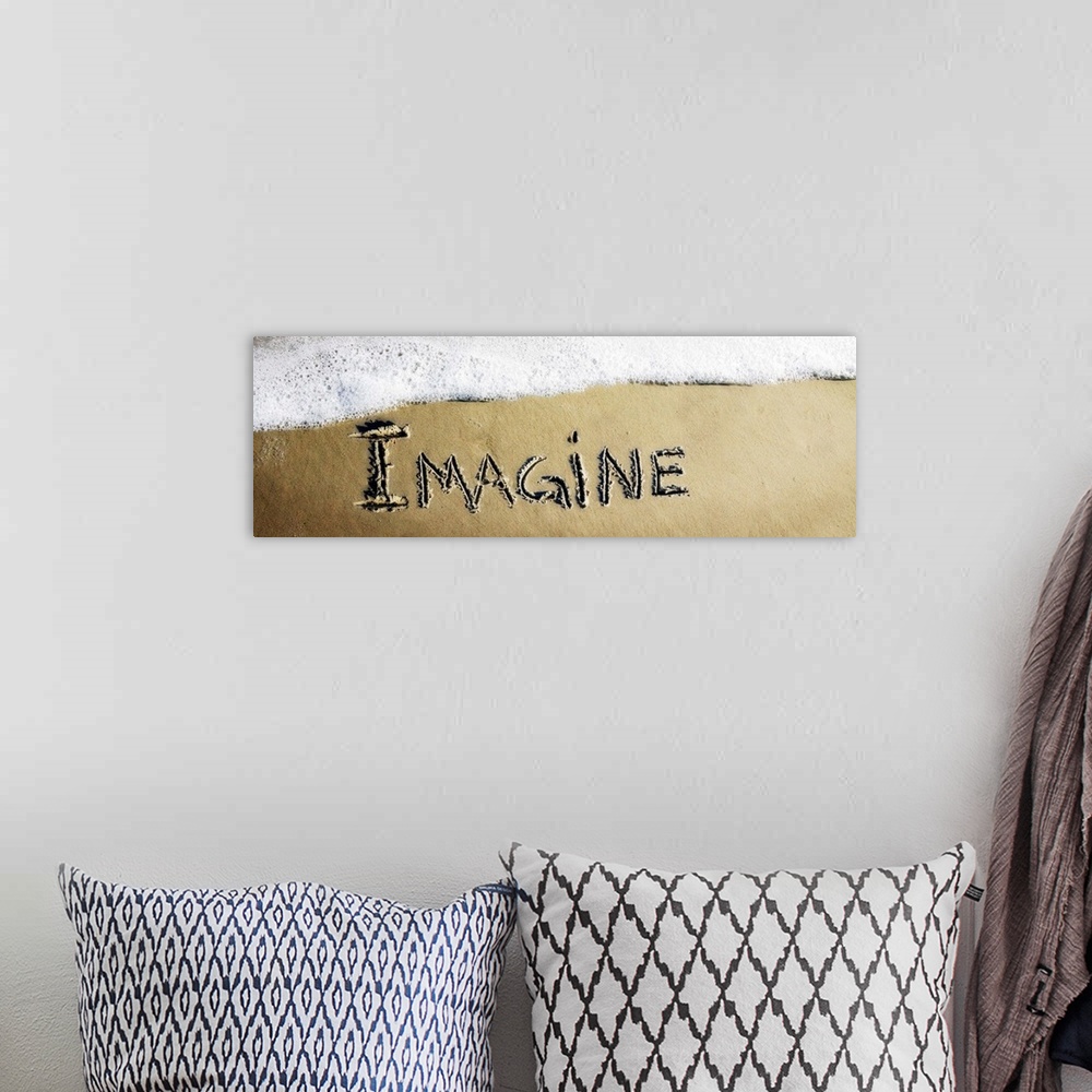 A bohemian room featuring The word "Imagine" drawn in the sand near the ocean water.