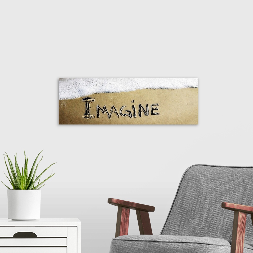A modern room featuring The word "Imagine" drawn in the sand near the ocean water.