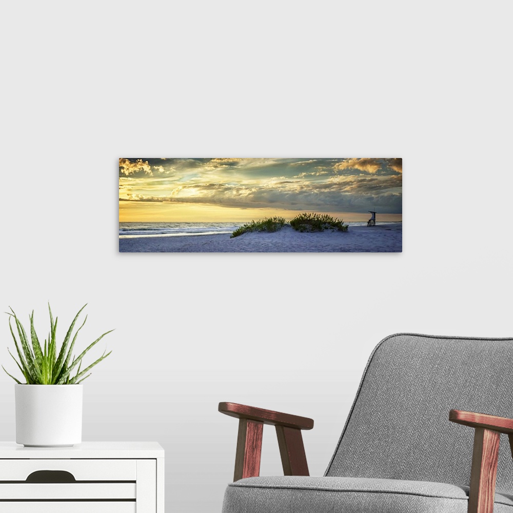 A modern room featuring Cloudy sky at sunrise glowing yellow over the beach.