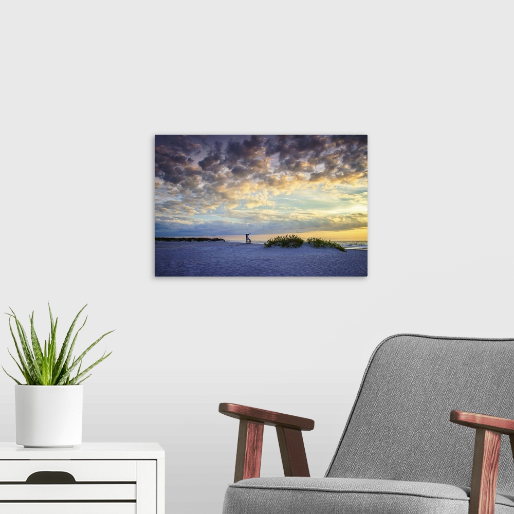 A modern room featuring Cloudy sky at sunrise glowing yellow and pale blue over the beach.