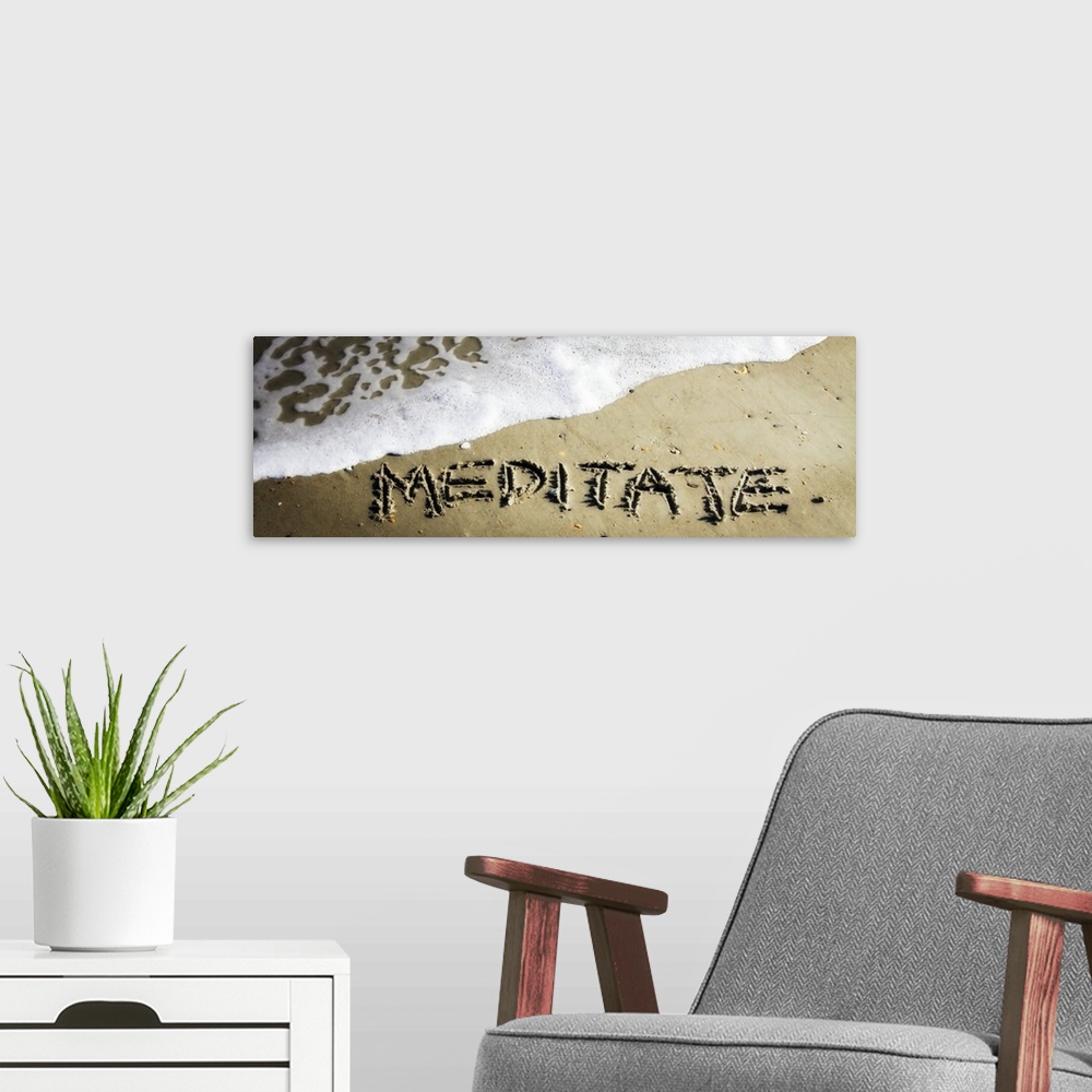 A modern room featuring The word "Meditate" drawn in the wet sand near ocean water.