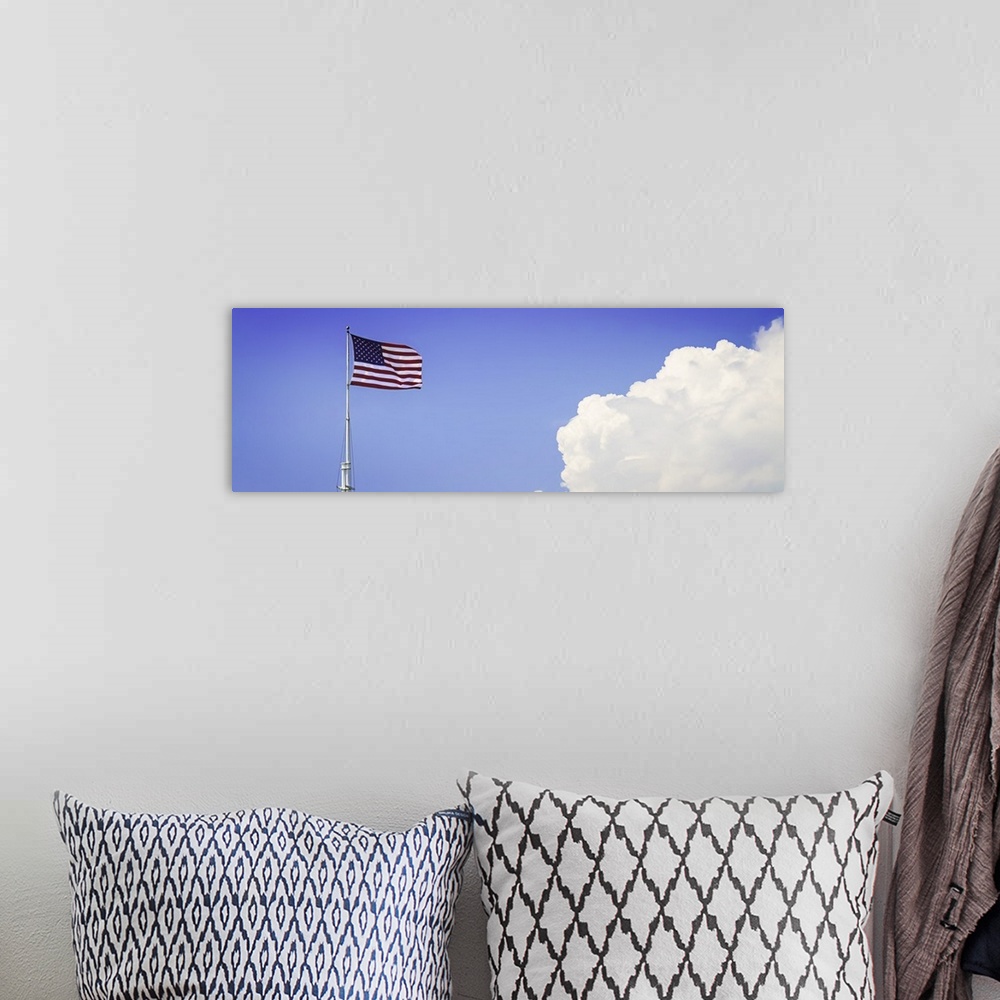 A bohemian room featuring American flag flying high with large clouds in the blue sky.
