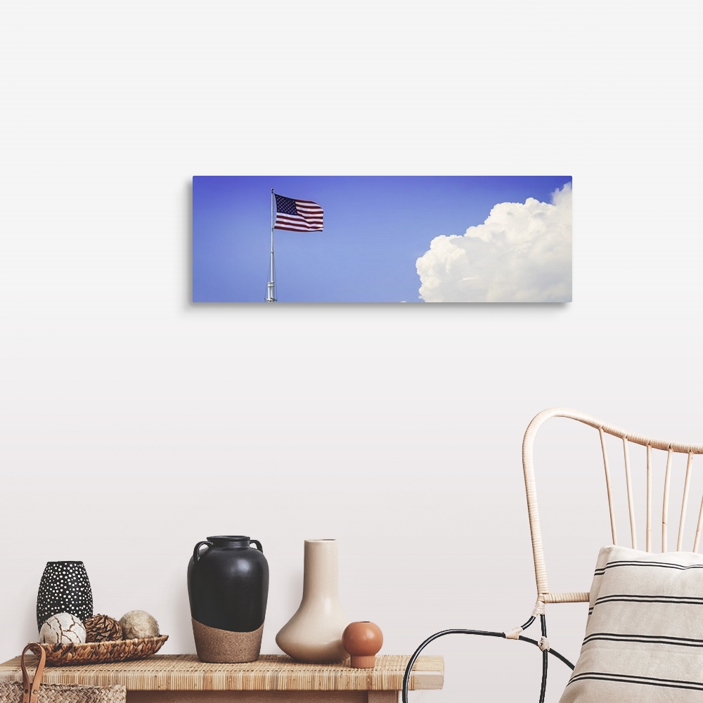 A farmhouse room featuring American flag flying high with large clouds in the blue sky.