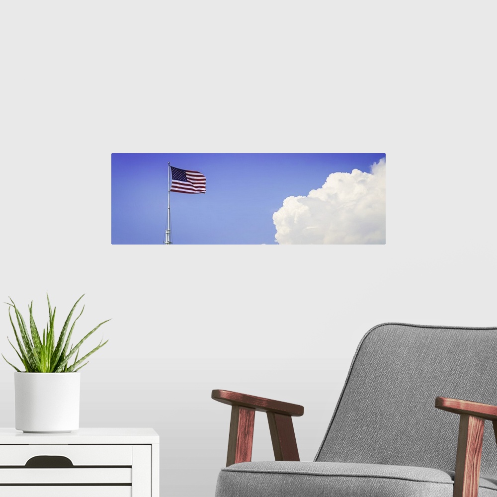 A modern room featuring American flag flying high with large clouds in the blue sky.