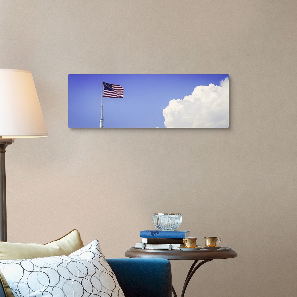 A traditional room featuring American flag flying high with large clouds in the blue sky.