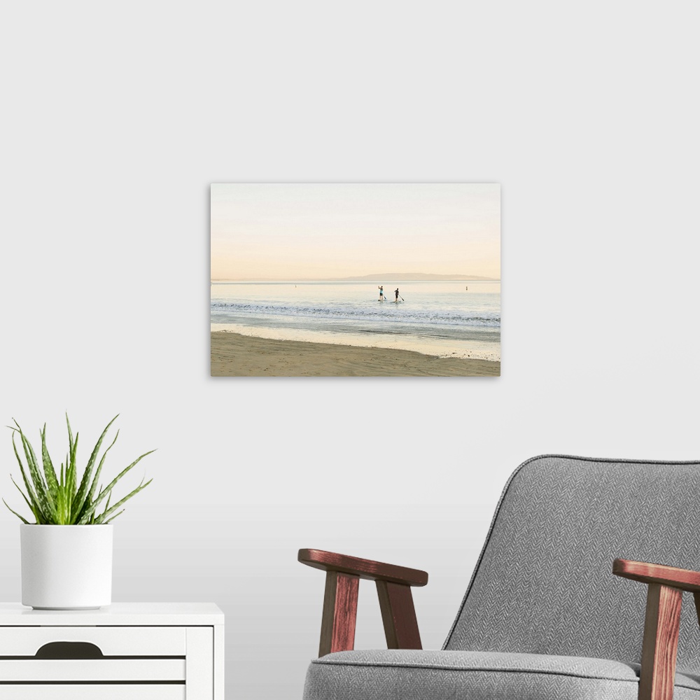 A modern room featuring Two paddleboarders in the ocean, seen from the shore.