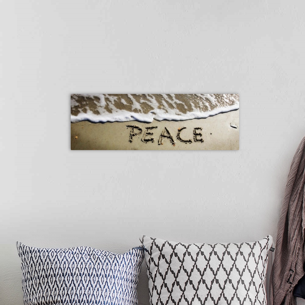 A bohemian room featuring The word "Peace" drawn in the wet sand near ocean water.