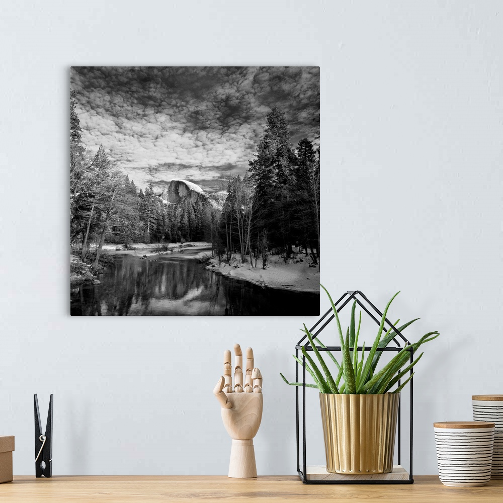 A bohemian room featuring Square black and white landscape photograph of a body of water lined with snow and trees with a l...