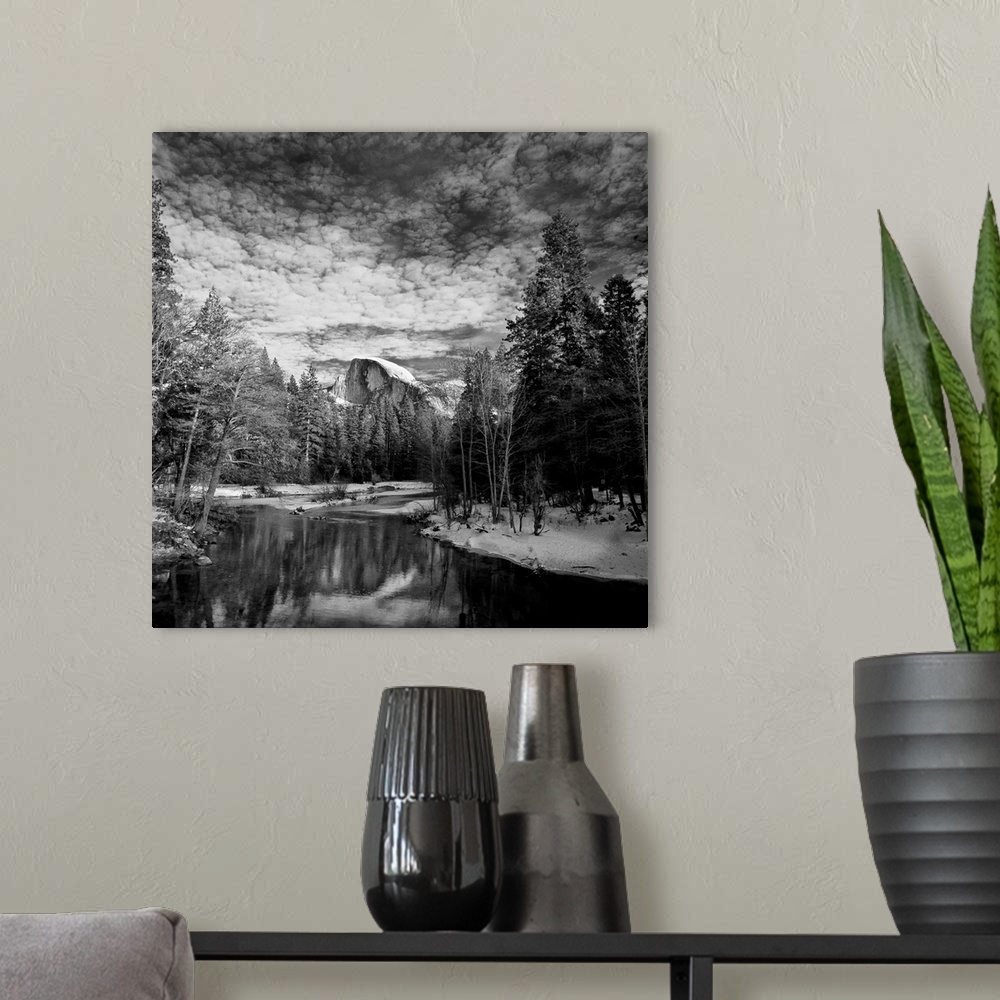A modern room featuring Square black and white landscape photograph of a body of water lined with snow and trees with a l...