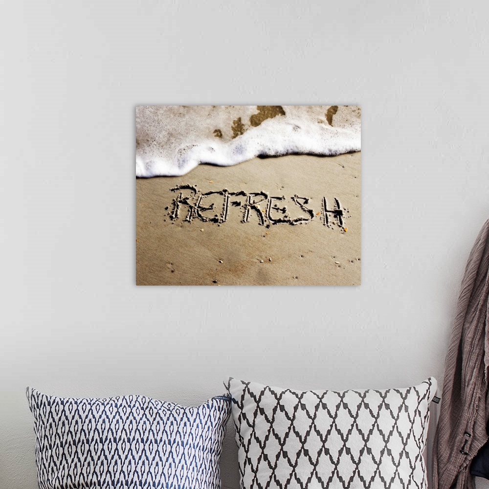 A bohemian room featuring The word "Refresh" drawn in the sand near the ocean water.