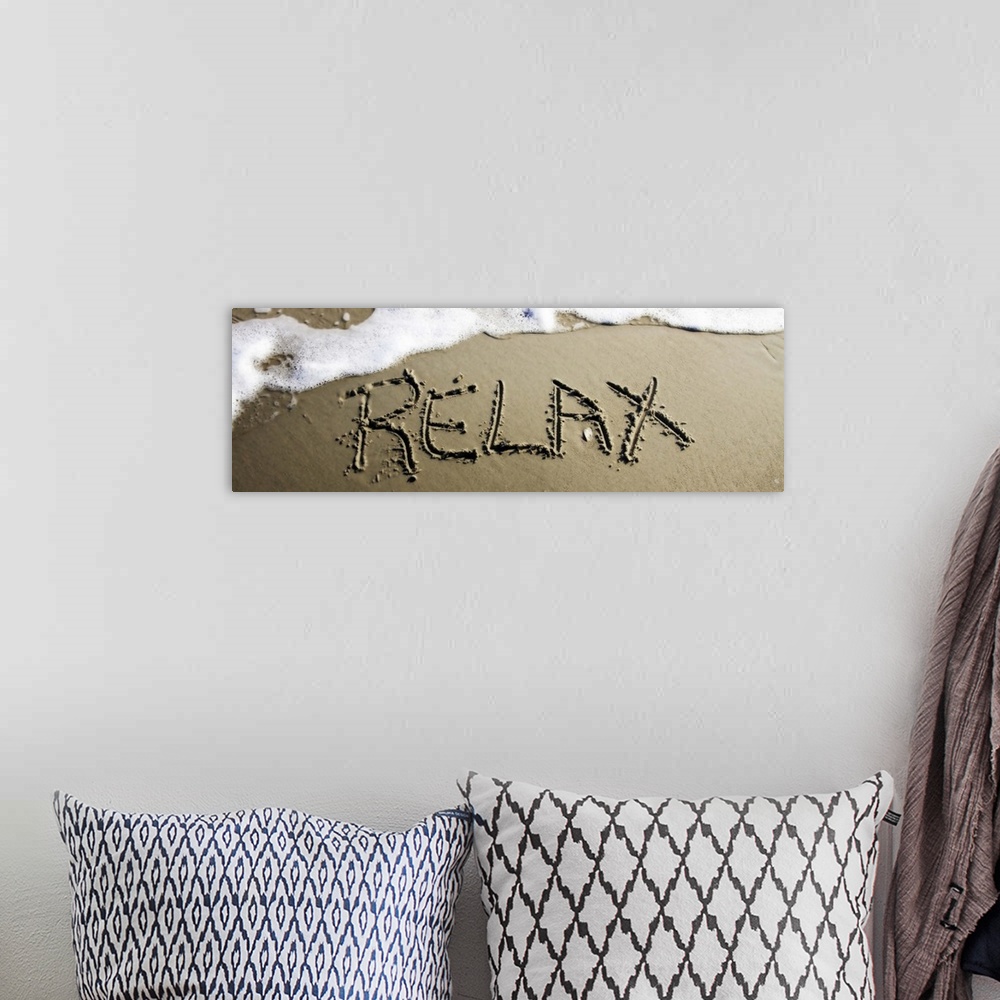 A bohemian room featuring The word "Relax" drawn in the wet sand near ocean water.