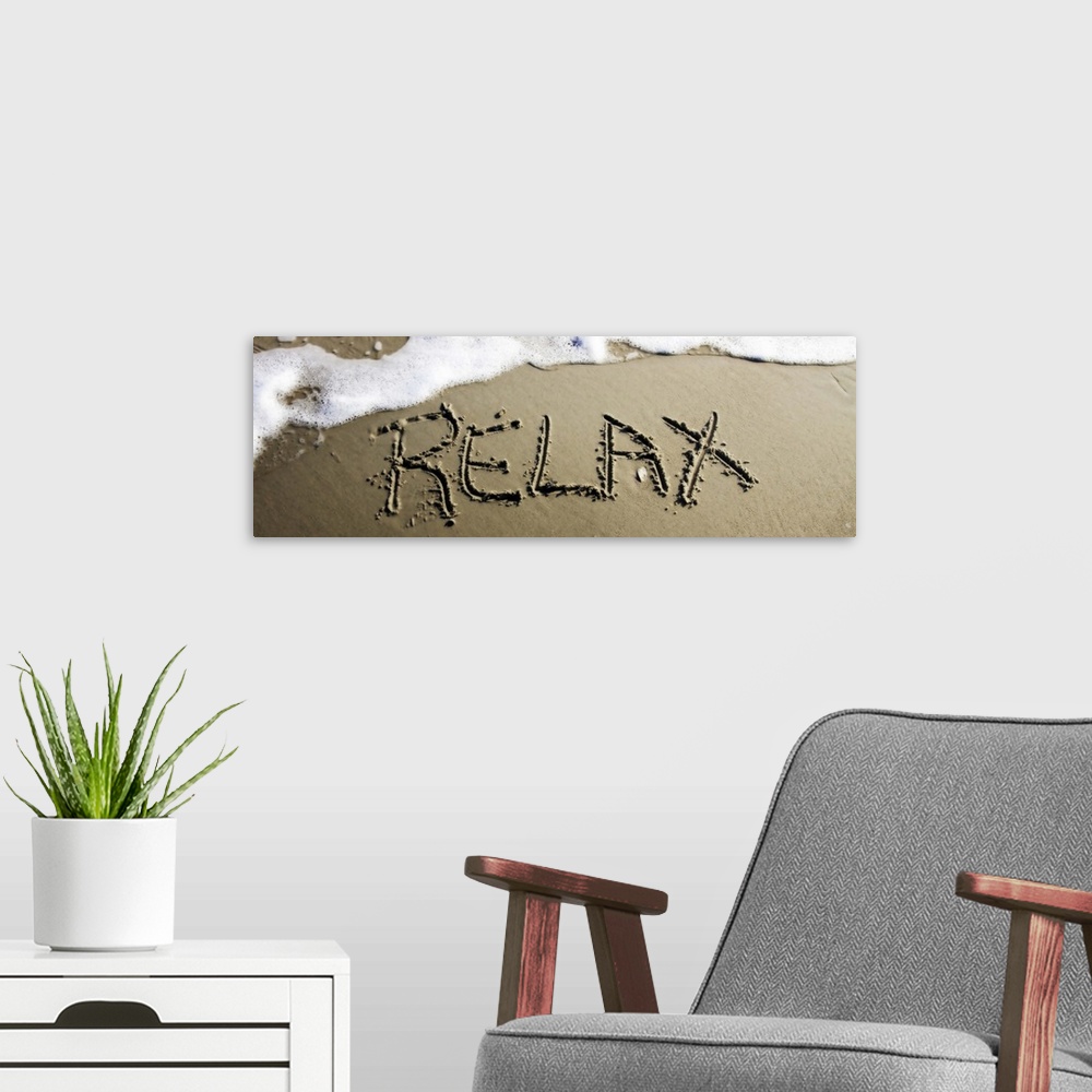 A modern room featuring The word "Relax" drawn in the wet sand near ocean water.