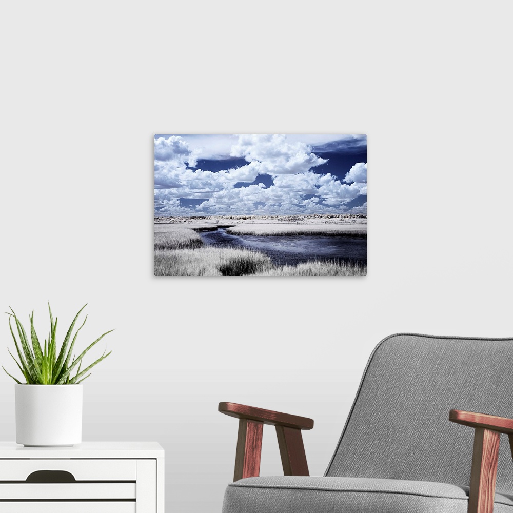 A modern room featuring Cool toned photograph of a deep blue river winding through a marsh with beautiful, white, fluffy ...