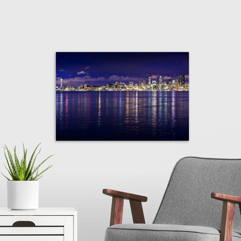 A modern room featuring Panoramic photograph of cityscape with waterfront at night.  The buildings are lit up and the lig...