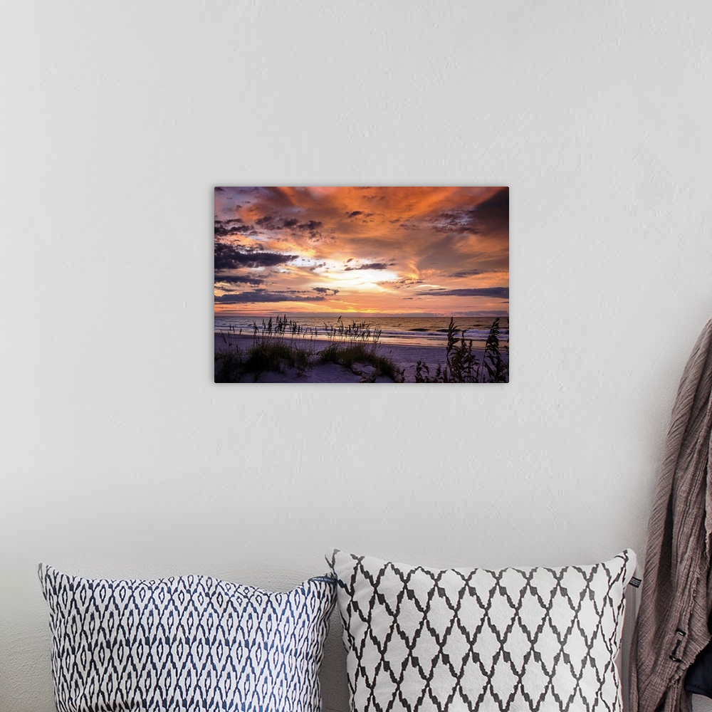 A bohemian room featuring Cloudy sky at sunrise glowing orange over the beach.