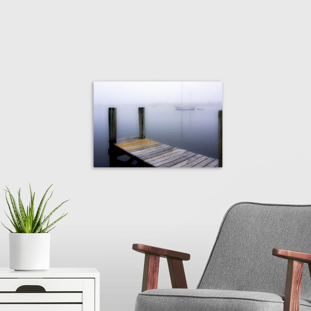 A modern room featuring Giant, horizontal wall picture of a wooden dock leading into calm water, several boats can be see...