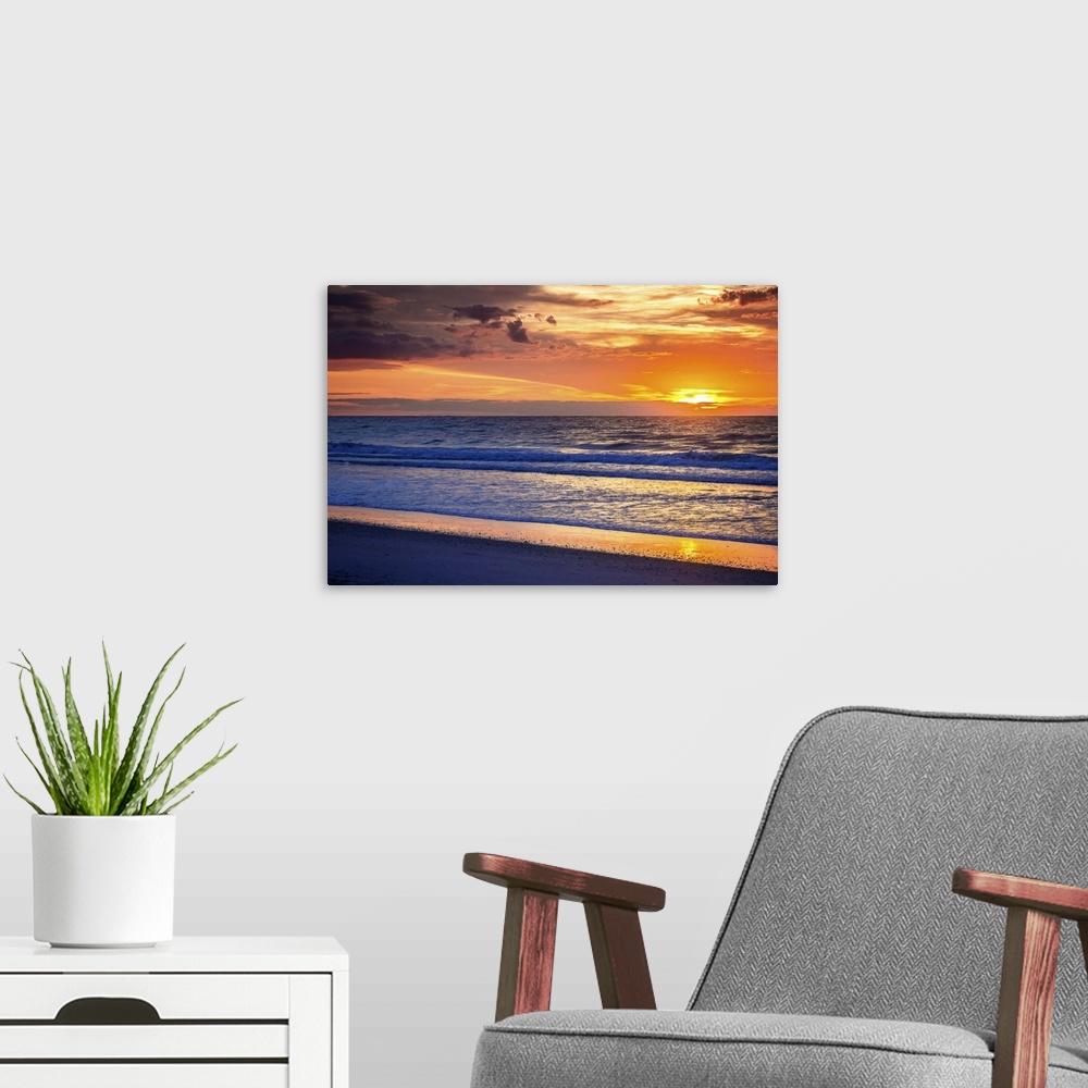 A modern room featuring Cloudy sky at sunrise glowing orange over the beach.