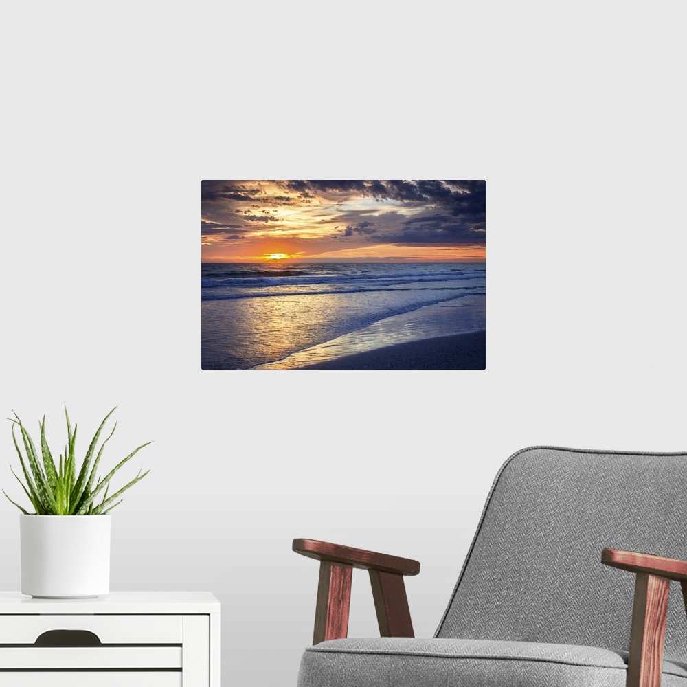 A modern room featuring Cloudy sky at sunrise glowing orange over the beach.