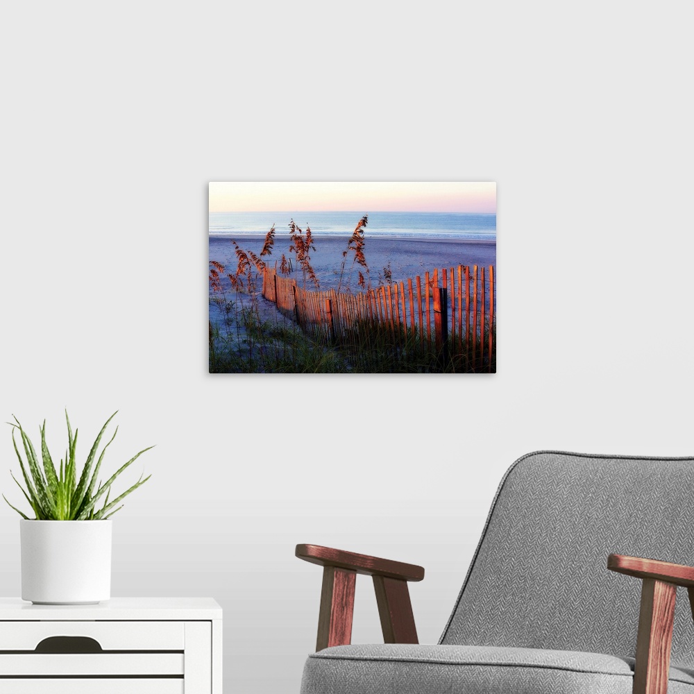 A modern room featuring Large photograph highlights a warm sunrise as it shines onto the fence and high grass in the fore...