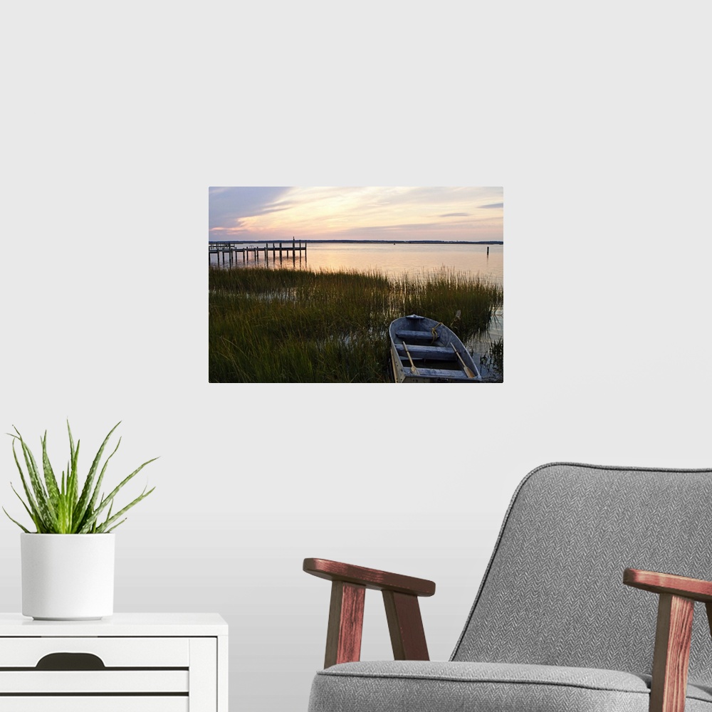 A modern room featuring A boat sits in shallow water amidst tall grass at dusk by a pier as calm waters reflect the sun's...
