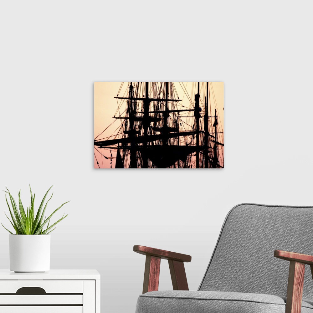 A modern room featuring A beautiful picture taken of the tops of ships that are silhouetted by a sunset sky as the backdrop.
