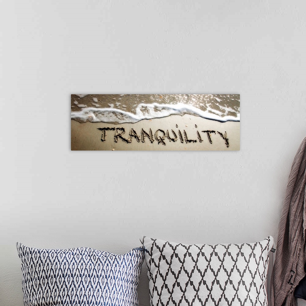 A bohemian room featuring The word "Tranquility" drawn in the wet sand near ocean water.