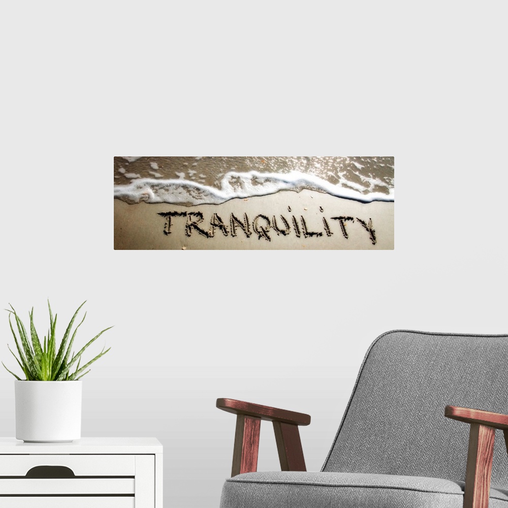 A modern room featuring The word "Tranquility" drawn in the wet sand near ocean water.