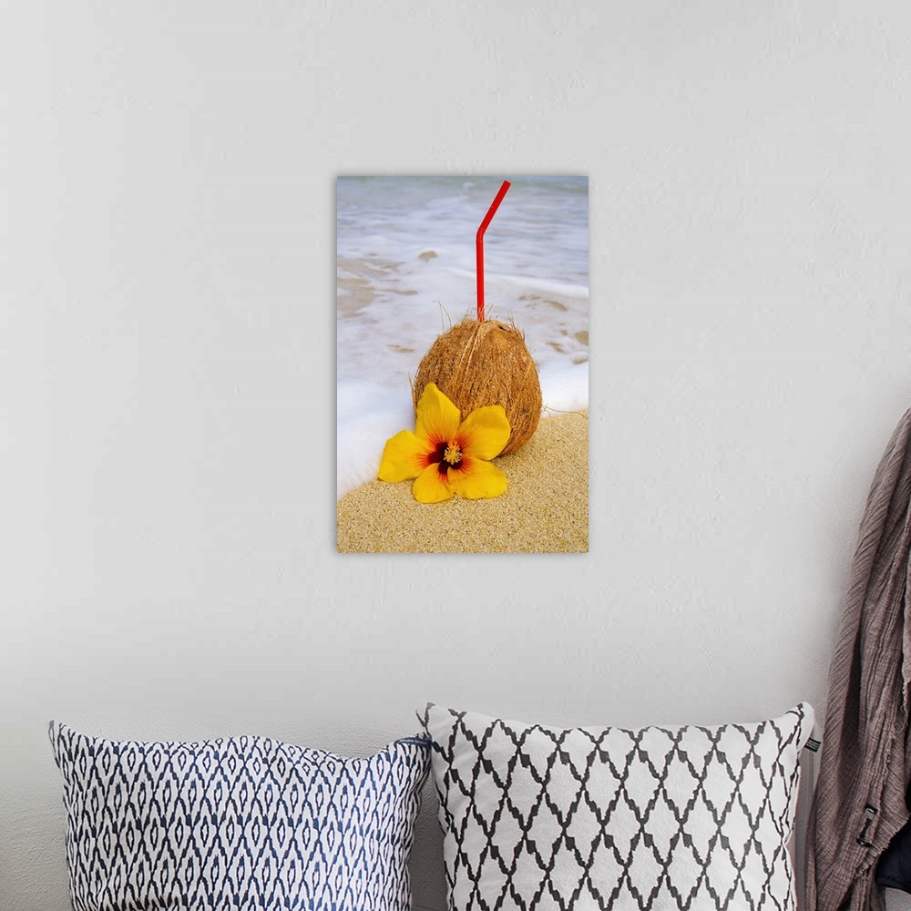 A bohemian room featuring A coconut drink with straw sticking out and flowers on a tropical beach.