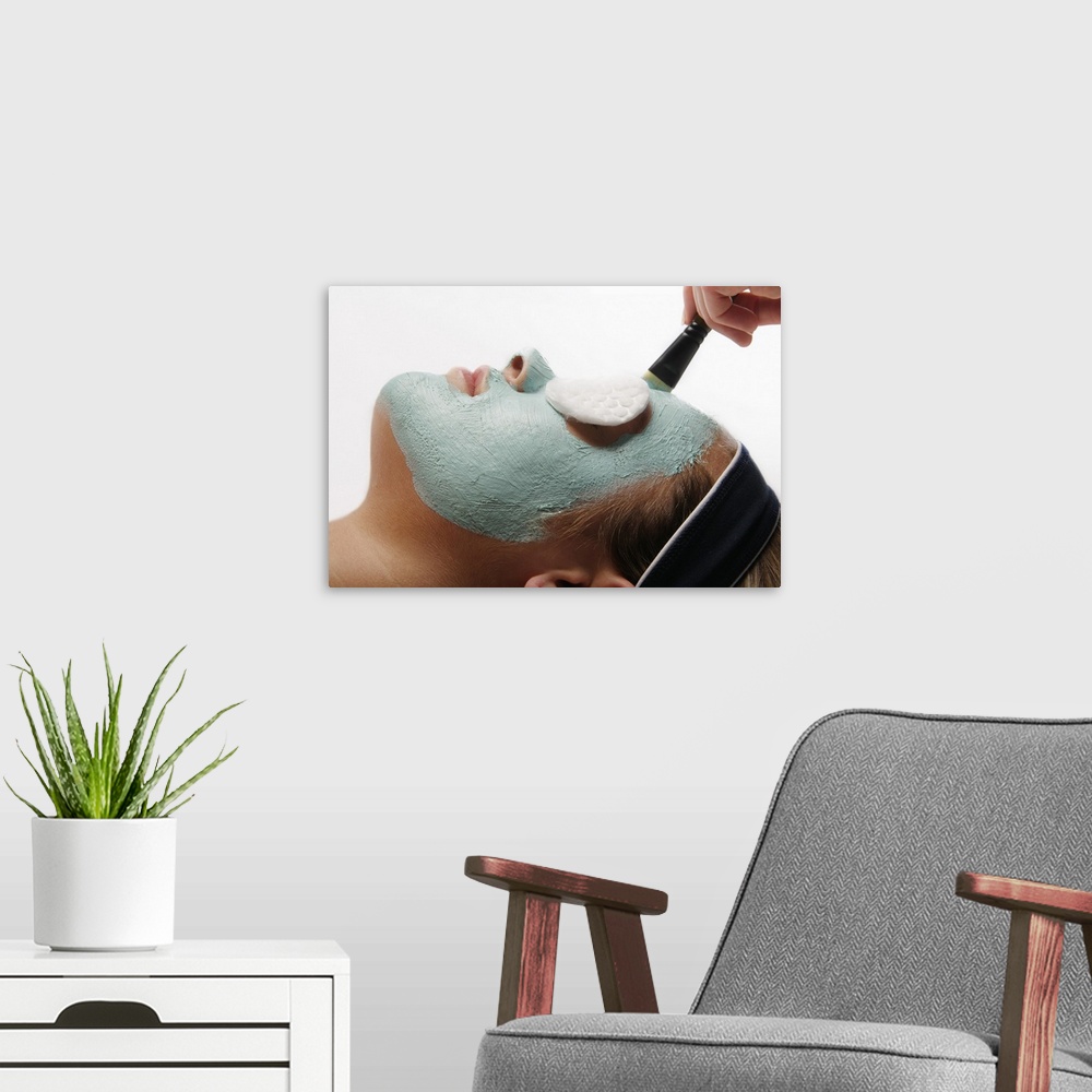 A modern room featuring Photograph of woman's face with clay mask and sponge covered eyes.
