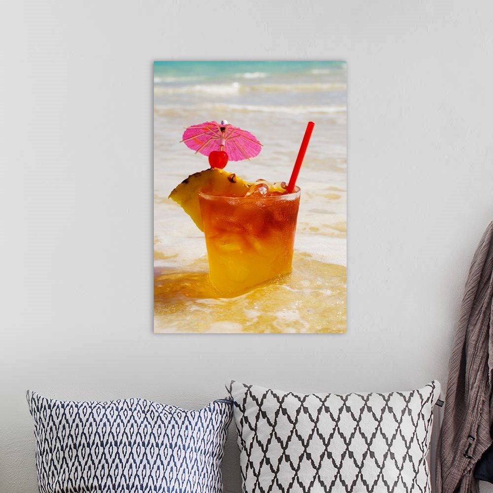 A bohemian room featuring A mai tai garnished with pinapple and a cherry, sitting in shallow water on the beach.