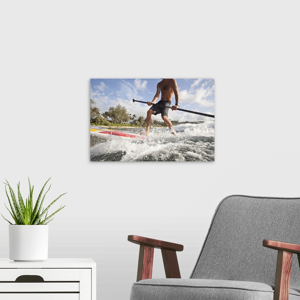 A modern room featuring Low angle view of a young man riding an ocean wave on a stand up paddle board