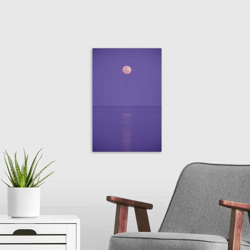 A modern room featuring a pink full moon hangs centered over a still body of water in the purple night