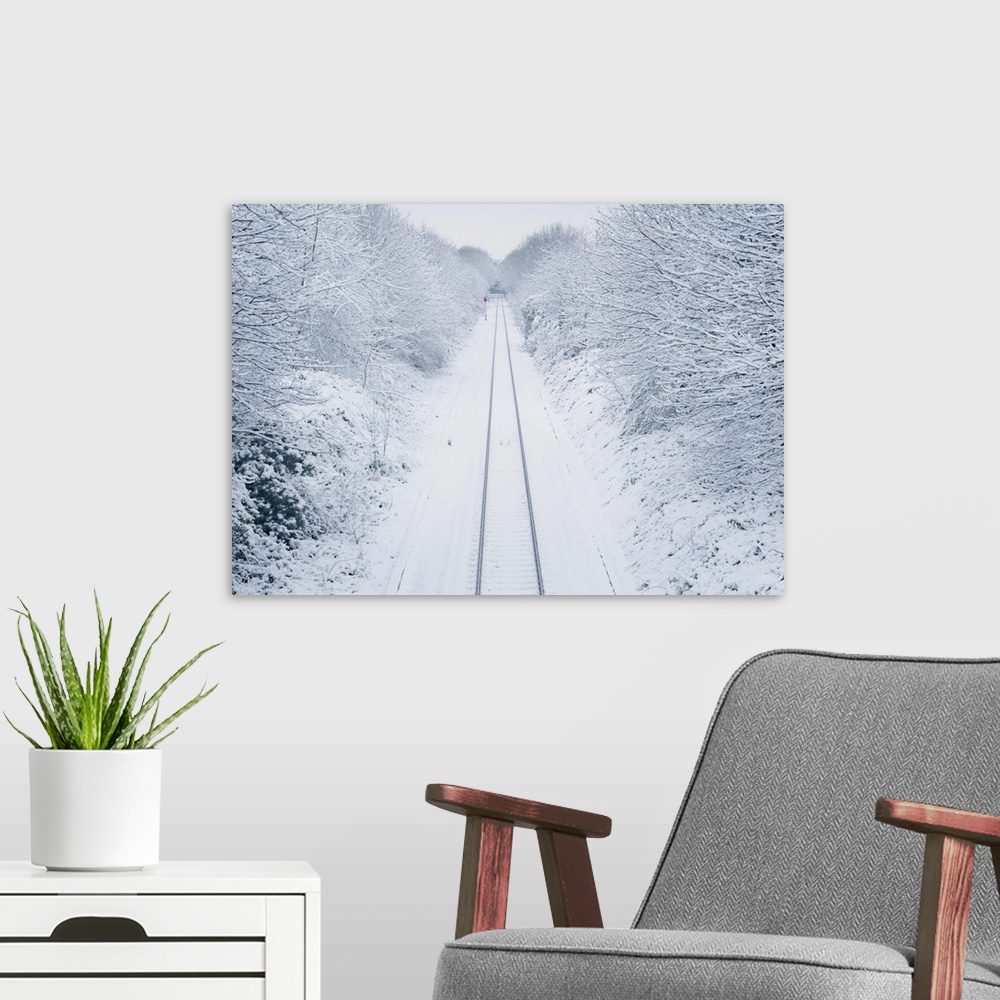 A modern room featuring A view overlooking a snow covered railway line as it vanishes past a lone red signal in the dista...