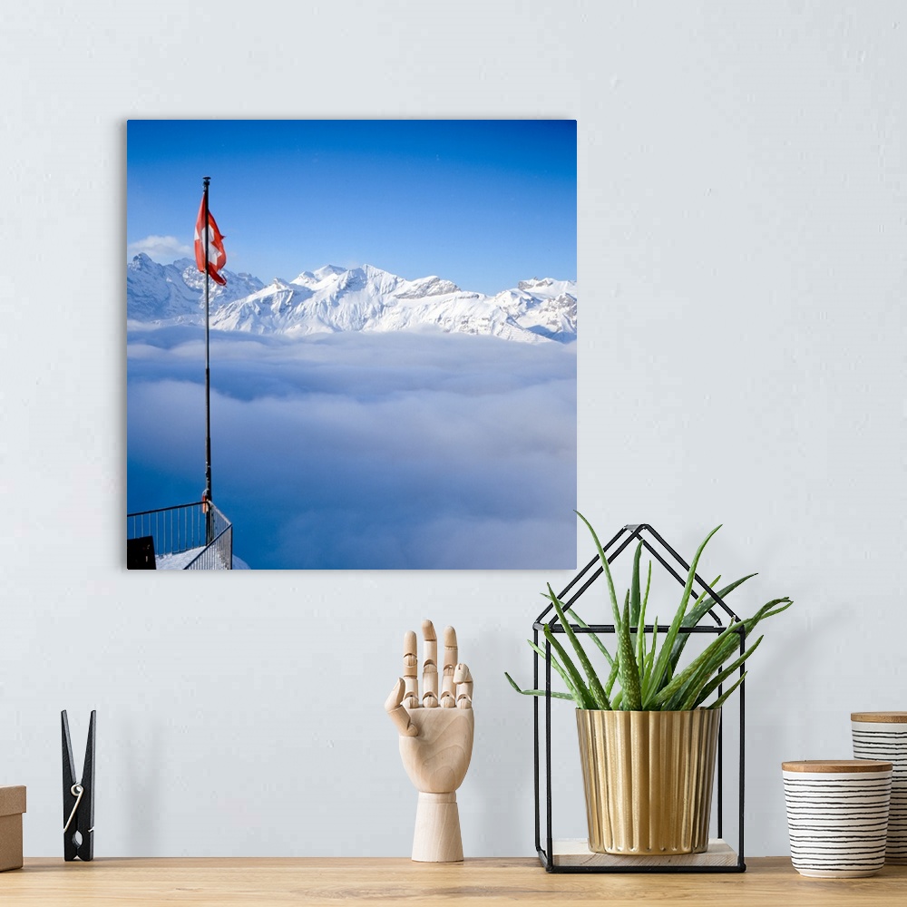A bohemian room featuring Above-the-clouds panorama shot of Swiss Alps, Swiss flag can be seen in foreground.