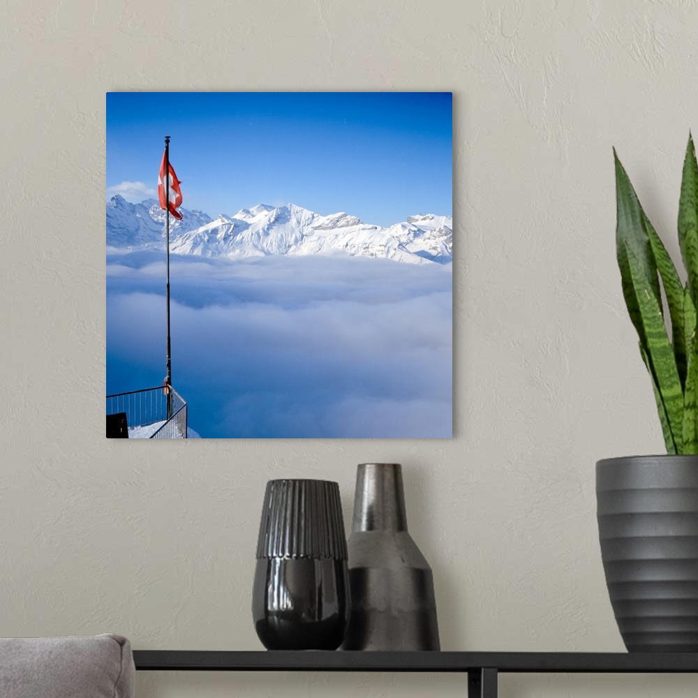 A modern room featuring Above-the-clouds panorama shot of Swiss Alps, Swiss flag can be seen in foreground.