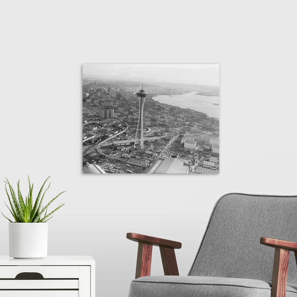 A modern room featuring An aerial view of Seattle prior to the World's Fair shows the new Space Needle and monorail snaki...