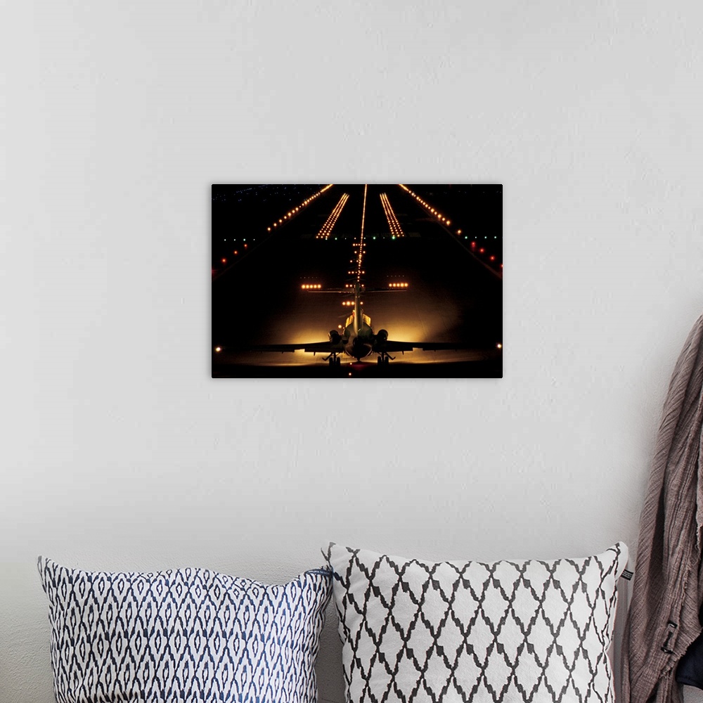 A bohemian room featuring Giant photograph shows a small aircraft stationed at the end of a brightly lit airstrip at nightt...